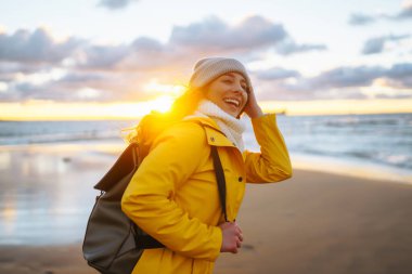 Sarı ceketli mutlu turist gün batımında deniz kenarında poz veriyor. Seyahat, yaşam tarzı, macera.