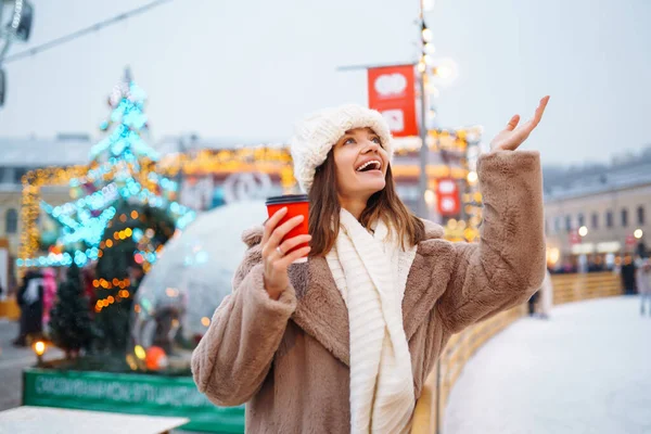 Stock image Young woman with coffee in winter over outdoor ice skating rink on background. Festive Christmas fair, winter holidays concept.