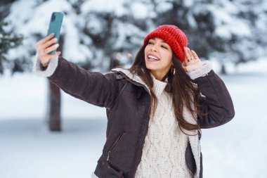 Genç bir kadın kış ormanında selfie çekiyor. Tatiller, dinlenme, seyahat konsepti.