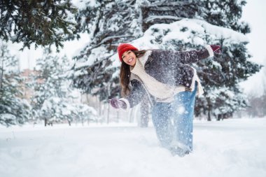 Genç kadın gülüyor ve kışın karlı bir parka kar atıyor. Tatiller, dinlenme, seyahat konsepti.