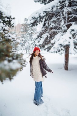 Genç kadın gülüyor ve kışın karlı bir parka kar atıyor. Tatiller, dinlenme, seyahat konsepti.