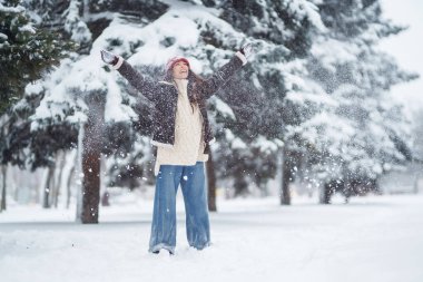 Genç kadın gülüyor ve kışın karlı bir parka kar atıyor. Tatiller, dinlenme, seyahat konsepti.