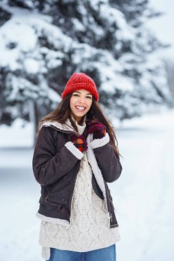 Genç kadın gülüyor ve kışın karlı bir parka kar atıyor. Tatiller, dinlenme, seyahat konsepti.