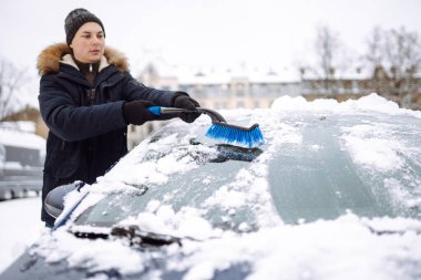 Arabadan karı fırçayla temizleyen genç adam. Ulaşım, kış, hava, insan ve araç kavramı.