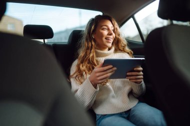 Arabanın arka koltuğunda elinde tabletle oturan genç ve güzel bir kadın. İş, teknoloji, internet, çevrimiçi konser. 