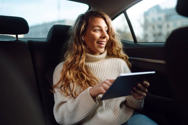 Young beautiful woman sitting in the back seat of the car with a tablet in hand. Business, technologie, internet, online concert.