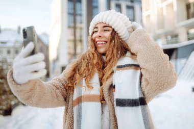 Kış sokağında selfie çeken genç bir kadın. Tatiller, dinlenme, blog yazma.