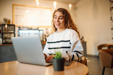 Young woman sits in a cafe and works on a computer. Business, blogging, freelance, education concept.