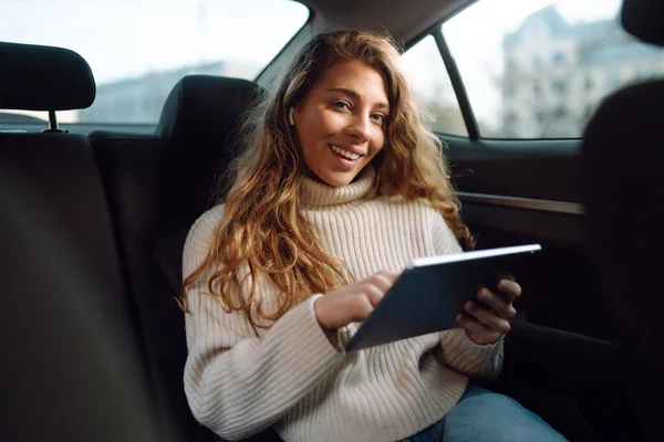 Beautiful woman sitting in the back seat of the car with a tablet in hand. Business, taxi, technologie, internet, online concert.
