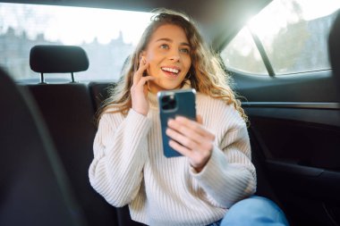 Young Woman using her phone during Traveling in a Car. Girl is checking Mails, Chats while she rides in a Taxi. Business, technology, blogging concept. 