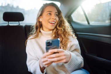 Young Woman using her phone during Traveling in a Car. Girl is checking Mails, Chats while she rides in a Taxi. Business, technology, blogging concept. 