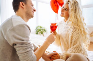 Young couple at home celebrating Valentine's Day  with glass of red wine. Romantic day together. Relationship, surprise and love concept.