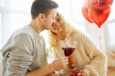 Young couple at home celebrating Valentine's Day  with glass of red wine. Romantic day together. Relationship, surprise and love concept.