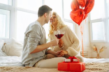 Young couple at home celebrating Valentine's Day  with glass of red wine. Romantic day together. Relationship, surprise and love concept.