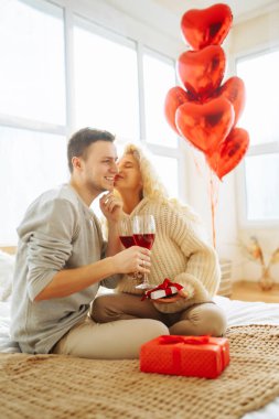 Young couple at home celebrating Valentine's Day  with glass of red wine. Romantic day together. Relationship, surprise and love concept.
