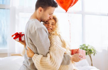 Beautiful young couple at home celebrating Valentine's Day. Exchange of gifts.  Relationship, surprise and love concept.