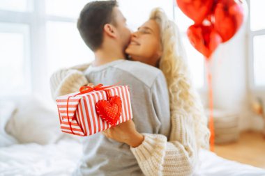 Beautiful young couple at home celebrating Valentine's Day. Exchange of gifts.  Relationship, surprise and love concept.