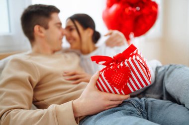 Beautiful young couple at home celebrating Valentine's Day. Exchange of gifts.  Relationship, surprise and love concept.