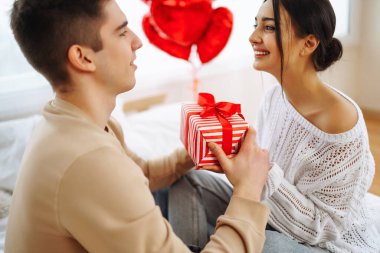 Beautiful young couple at home celebrating Valentine's Day. Exchange of gifts.  Relationship, surprise and love concept.