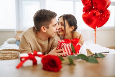 Beautiful young couple at home celebrating Valentine's Day. Exchange of gifts.  Relationship, surprise and love concept.