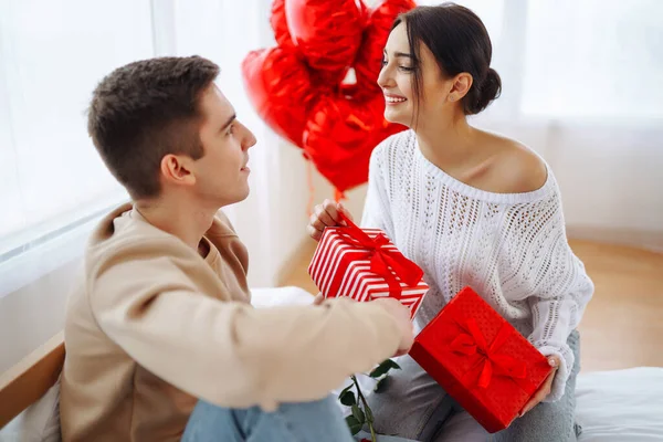 Beautiful young couple at home celebrating Valentine's Day. Exchange of gifts.  Relationship, surprise and love concept.