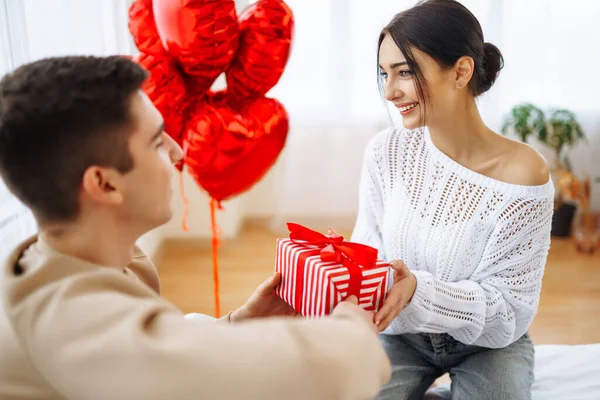Beautiful young couple at home celebrating Valentine's Day. Exchange of gifts.  Relationship, surprise and love concept.