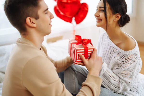 Beautiful young couple at home celebrating Valentine's Day. Exchange of gifts.  Relationship, surprise and love concept.