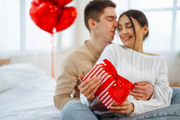 Beautiful young couple at home celebrating Valentine's Day. Exchange of gifts.  Relationship, surprise and love concept.