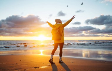 Happy tourist in a yellow jacket enjoying sea landscape at sunset. Lifestyle, travel, tourism, nature, active life.