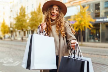 Alışveriş torbalı şık bir kadın şehrin sokaklarında yürüyor. Bahar stili. Tüketim, satın alma, alışveriş, yaşam tarzı konsepti.