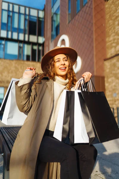 Stylish woman with shopping bags walks through the city streets. Spring Style. Consumerism, purchases, shopping, lifestyle concept.