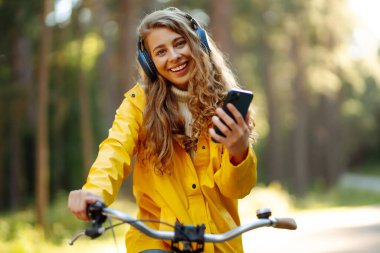Pretty young womanusing mobile phone in the city while listening music through earphones to go by the bicycle in the park. Lifestyle. Relax, nature concept.