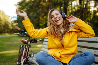 Pretty young womanusing mobile phone in the city while listening music through earphones to go by the bicycle in the park. Lifestyle. Relax, nature concept.