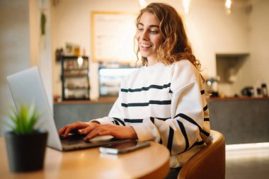 Woman sitting  in cafe  with laptop, typing text message using smart phone while working.Technology, Freelance, online course, remote work, internet concept.