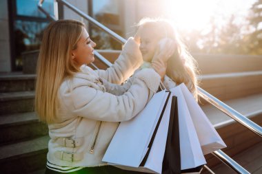 Happy mother and daughter with shopping bags walking along city street. sale, consumerism and people concept