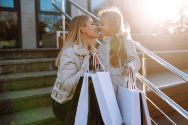 Happy mother and daughter with shopping bags walking along city street. sale, consumerism and people concept