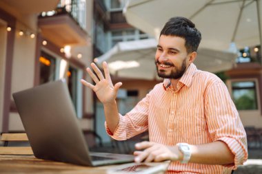 Bilgisayarı ve telefonu olan genç bir adam bir kafede oturuyor ve çalışıyor. İş, blog yazma, serbest çalışma, eğitim kavramı.