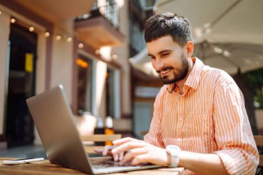 Bilgisayarı ve telefonu olan genç bir adam bir kafede oturuyor ve çalışıyor. İş, blog yazma, serbest çalışma, eğitim kavramı.