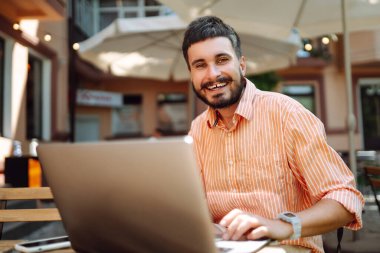 Bilgisayarı ve telefonu olan genç bir adam bir kafede oturuyor ve çalışıyor. İş, blog yazma, serbest çalışma, eğitim kavramı.