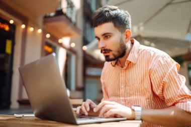 Bilgisayarı ve telefonu olan genç bir adam bir kafede oturuyor ve çalışıyor. İş, blog yazma, serbest çalışma, eğitim kavramı.