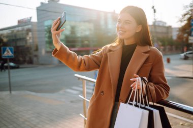 Telefonunu kullanarak alışveriş torbalarıyla gülümseyen kadın. Satın almalar, kara cuma, indirimler, satış konsepti. Çevrimiçi alışveriş kavramı.