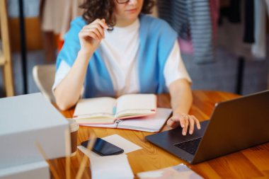 Genç bayan tasarımcı iş yerinde dizüstü bilgisayarla oturuyor. Küçük işletme sahibi, girişimci, ecommerce giyim mağazasının siparişlerini kontrol eden satıcı. Alışveriş konsepti. Moda stüdyosu.