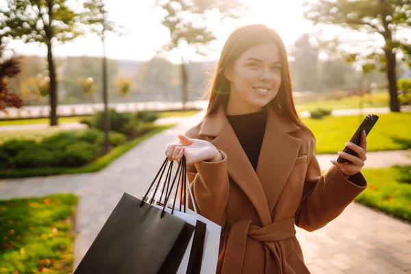 携帯電話で買い物袋を持った笑顔の女性 黒の金曜日 販売の概念 オンラインショッピングのコンセプト — ストック写真