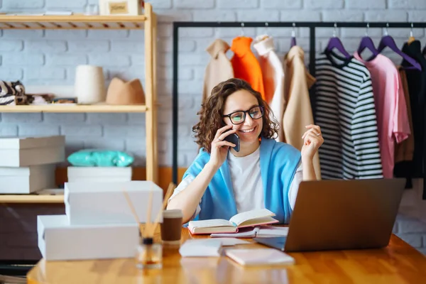 Genç bayan tasarımcı iş yerinde dizüstü bilgisayarla oturuyor. Küçük işletme sahibi, girişimci, ecommerce giyim mağazasının siparişlerini kontrol eden satıcı. Alışveriş konsepti. Moda stüdyosu.