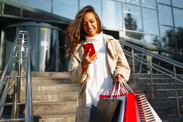 Jonge Vrouw Buurt Van Winkelcentrum Met Boodschappentassen Een Mobiele Telefoon — Stockfoto