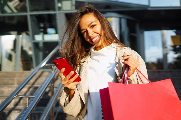 Ung Kvinna Står Nära Köpcentret Håller Shoppingväskor Och Använder Mobiltelefon — Stockfoto
