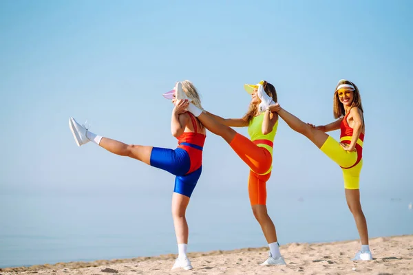 三个年轻的女舞蹈家穿着鲜艳的泳衣在海滩上跳舞 积极生活 — 图库照片