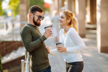 Genç bir çift sabah yürürken konuşuyor, kahve içiyor ve telefonla konuşuyor. Rahatlama, gençlik, aşk, yaşam tarzı, özçekim, blog yazma.