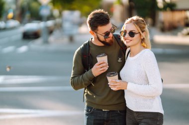 Genç bir çift sabah yürürken konuşuyor, kahve içiyor ve telefonla konuşuyor. Rahatlama, gençlik, aşk, yaşam tarzı, özçekim, blog yazma.