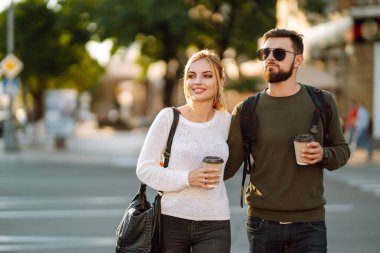 Genç bir çift sabah yürürken konuşuyor, kahve içiyor ve telefonla konuşuyor. Rahatlama, gençlik, aşk, yaşam tarzı, özçekim, blog yazma.